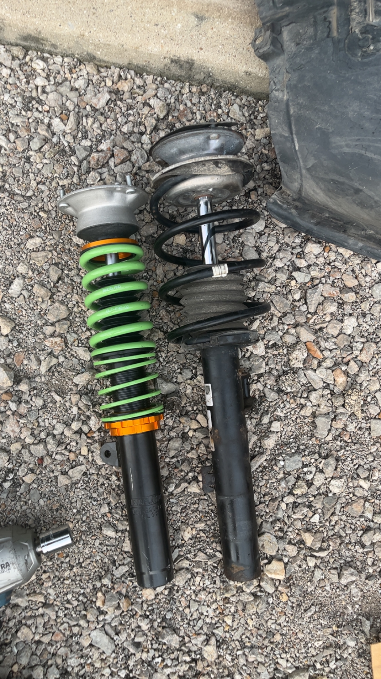 New green Raceland coilover next to a worn OEM strut assembly on gravel